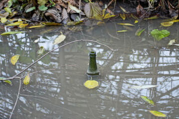 one green glass old bottle in the gray dirty lake water