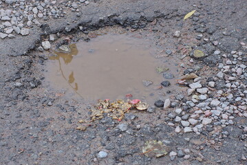 one large puddle of dirty water in a pothole on the asphalt on the road with earth and stones