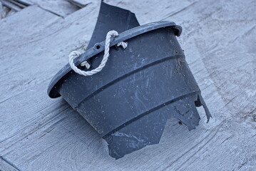 pieces of a black broken plastic bucket lie on a gray wooden table in the street © butus