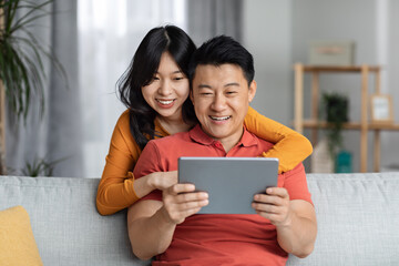 Happy asian lovers spending time together at home, using tablet