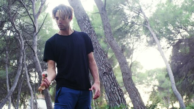Young male practicing kendama moves in the woods.