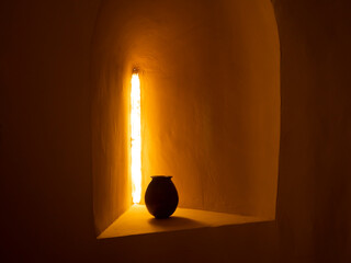 Old small vase in the dark in front of an old window with sunset light passing through. Antique historical art.