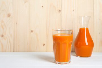 Tasty carrot juice on white wooden table, space for text