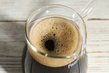 Glass turkish coffee pot with hot drink on wooden table, closeup