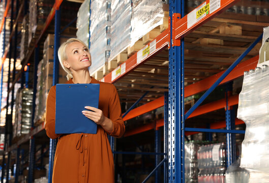 Happy manager holding clipboard in warehouse with lots of products, low angle view