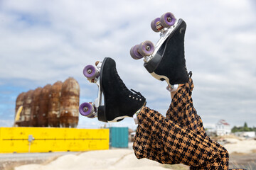 Roller skates raised in the air under blue sky with puffy white clouds. The wheels are purple