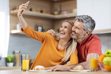 Joyful romantic couple taking selfie while having breakfast at home