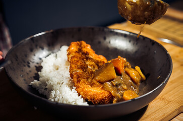 Japanese chicken katsu curry rice, deep fried breast chicken fillet with beef, carrot and potato curry in black plate on wooden table Crispy fried pork cutlet with curry rice  - Japanese food style