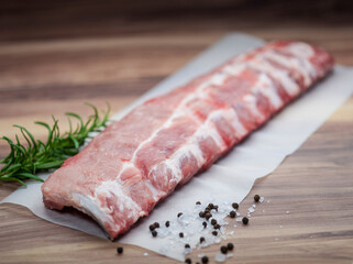 Spare ribs with rosemary, pepper and salt on parchment paper and wooden  background