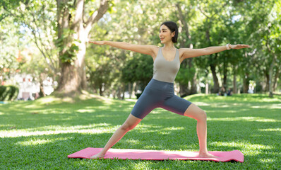 Young attractive girl is doing advanced yoga asana on the fitness mat in the middle of a park.