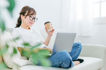 家でパソコンを使ってネットショッピングするメガネをかけたアジア人女性（笑顔）
