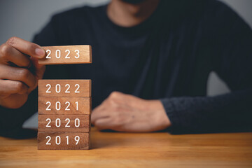 Happy New Year 2023. Businessman hand holding years 2023 number wooden block to put it above the...