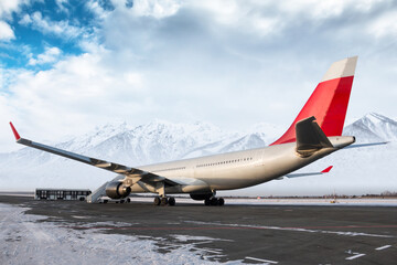 Wide body passenger airliner with staircase at the airport apron on the background of high scenic snow-capped mountains. Shuttle bus near the aircraft