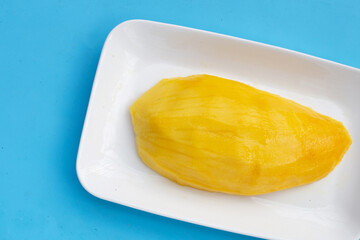 Yellow mango slices in white plate on blue background.