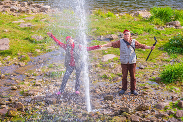 tourists travelers on the banks of the Ay river near the high fountain of a geyser on a summer...
