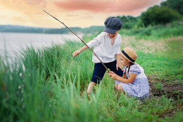 Two kids are fishing by the water. A boy and a girl with a fishing rod catch everything from the lake.