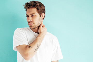 Portrait of handsome confident stylish hipster lambersexual model. Sexy man dressed in white T-shirt and jeans. Fashion male isolated on blue wall in studio. Mockup