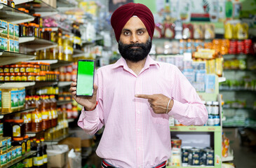 indian small business owner Showing mobile and pointing towards it 