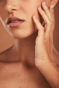 Hand, face and skincare with a closeup woman touching her skin in studio on a beige background for wellness or treatment. Cosmetics, luxury and beauty with a female inside to promote natural care