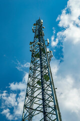 A tower for mobile communication antennas against a blue sky with white clouds. Mobile operator antennas. Radio communication tower. Internet and telephony. Internet business. The beauty.