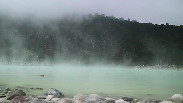 Spooky landscape with steam rising from green sulfur lake in Kawah Putih volcano crater in Bandung, Indonesia.