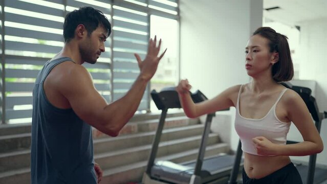 Beautiful young asian woman training boxing at finess class. Male coach giving a Private training to a female athlete practicing a punch.