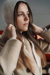 Elegant brunette woman with long hair wearing beige wool coat and cozy grey hat. Autumn trendy outdoor fashion