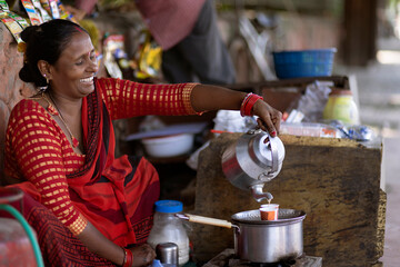 Female vendor pouring chai into cup for customer at a roadside stall