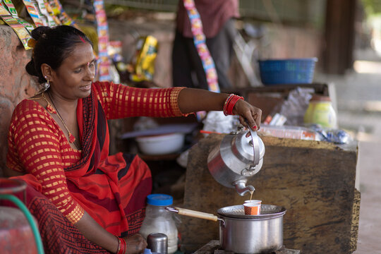 Female vendor pouring chai into cup for customer at a roadside stall