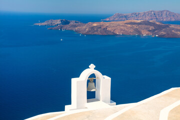 Fototapeta na wymiar Santorini, Greece. Composition with traditional white architecture and a bell against the backdrop of the blue sea and volcanic natural islands.