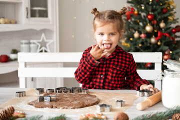 little girl in red pajama cooking festive gingerbread in christmas decorated kitchen