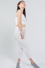 Young beautiful brown-haired girl in a white top and trousers posing on a white background