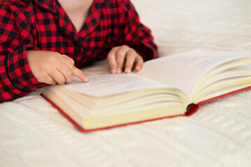 cute little girl in red Christmas pajama lying on bed reading book