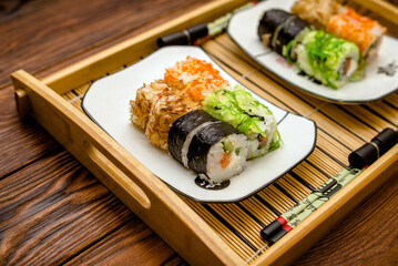 Several sushi on a white plate standing on a brown wooden background
