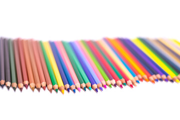 Colored pencils arranged in a curved line on a white background with a blurred background