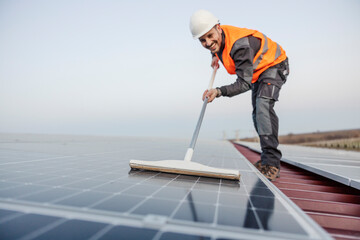 Neat worker in protective uniform is cleaning solar panels from dust.