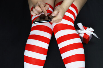 Girl in red striped knee socks sitting with smartphone in hands. Christmas holidays, online greetings