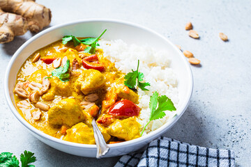 Thai chicken and peanut curry with rice in white bowl, gray background. Asian cuisine concept.