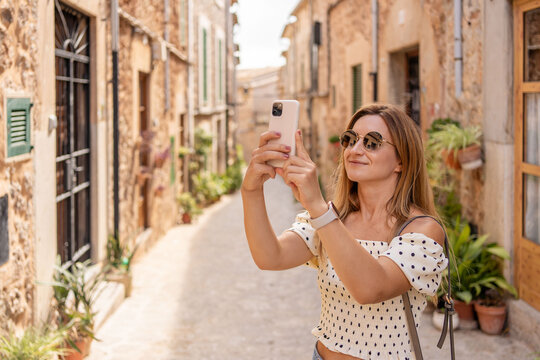 Young tourist woman using smartphone in the city, taking pictures. Girl makes a photo on the streets of the old town on a summer sunny day. Girl using cell phone photography app.