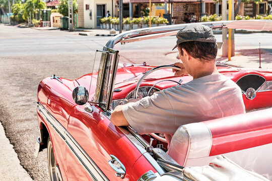 Man Sitting In Red Vintage 1957 Car On Street Of Resort Town Varadero, Cuba.