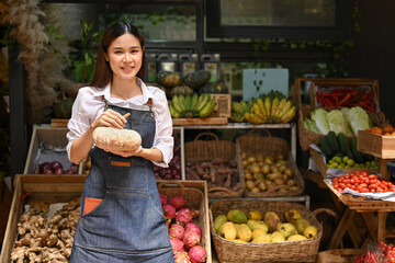 Portrait of young woman in apron standing front of her organic vegetable stall at an open street. Farmers market concept
