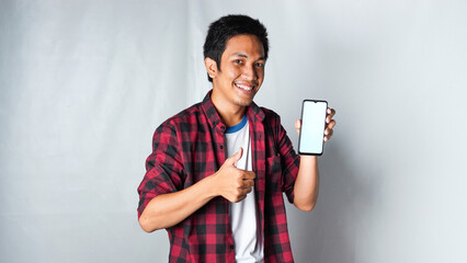 Adult Asian man wearing red flannel shirt smiling and give thumb up while holding mobile phone and OK hand gesture