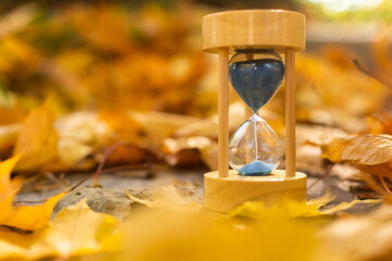 Hourglass and autumn leaves in the park. A symbol of passing time. Symbol of short life.