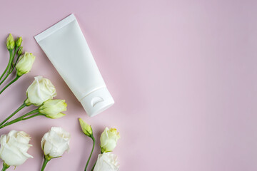Obraz na płótnie Canvas Moisturizer hand cream white plastic tube mockup on pink trandy background with eustoma flowers. Blank skin care beauty product packaging