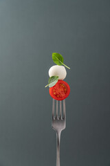 Fork with tomato, mozzarella cheese and basil. Caprese salad on fork close up view. Italian food...