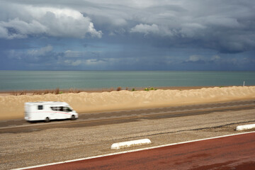 Motorhome on sand beach in motion. White camper driving on the road in front of the North Sea, in rainy weather. Holland, Zeeland, Brouwersdam.