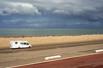 Photo sur Plexiglas Mer du Nord, Pays-Bas Motorhome on sand beach in motion. White camper driving on the road in front of the North Sea, in rainy weather. Holland, Zeeland, Brouwersdam.