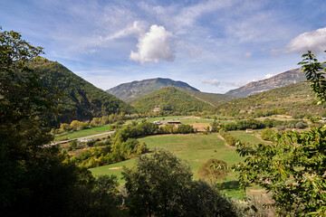 Obraz premium Aerial view of a meadow surrounded by mountains and vegetation with the sky with clouds at sunset very colorful