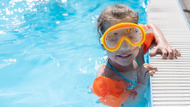 Portrait of a cute little Caucasian girl swimming in the pool wearing a diving mask and swimming headbands, beach resort, summer vacation concept. Space for text.