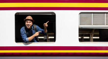 Young asian man travel by train. Sticking his head outta the train window. Explorer Backpacker arrival and departure at platform railway. Freedom  trip on vacation time holiday weekend.